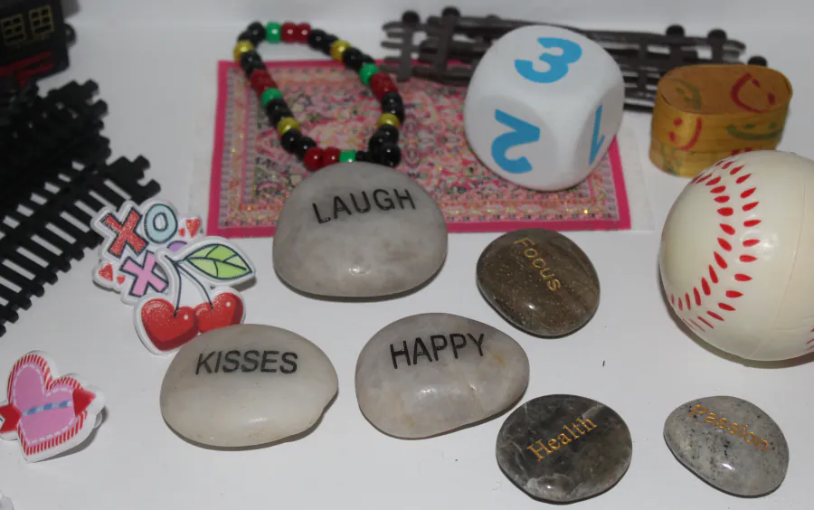 Expressive-therapy objects laid out on a table at the Centre — small painted stones reading &lsquo;laugh&rsquo;, &lsquo;kisses&rsquo; and &lsquo;happy&rsquo;, beads, dice, and figures.