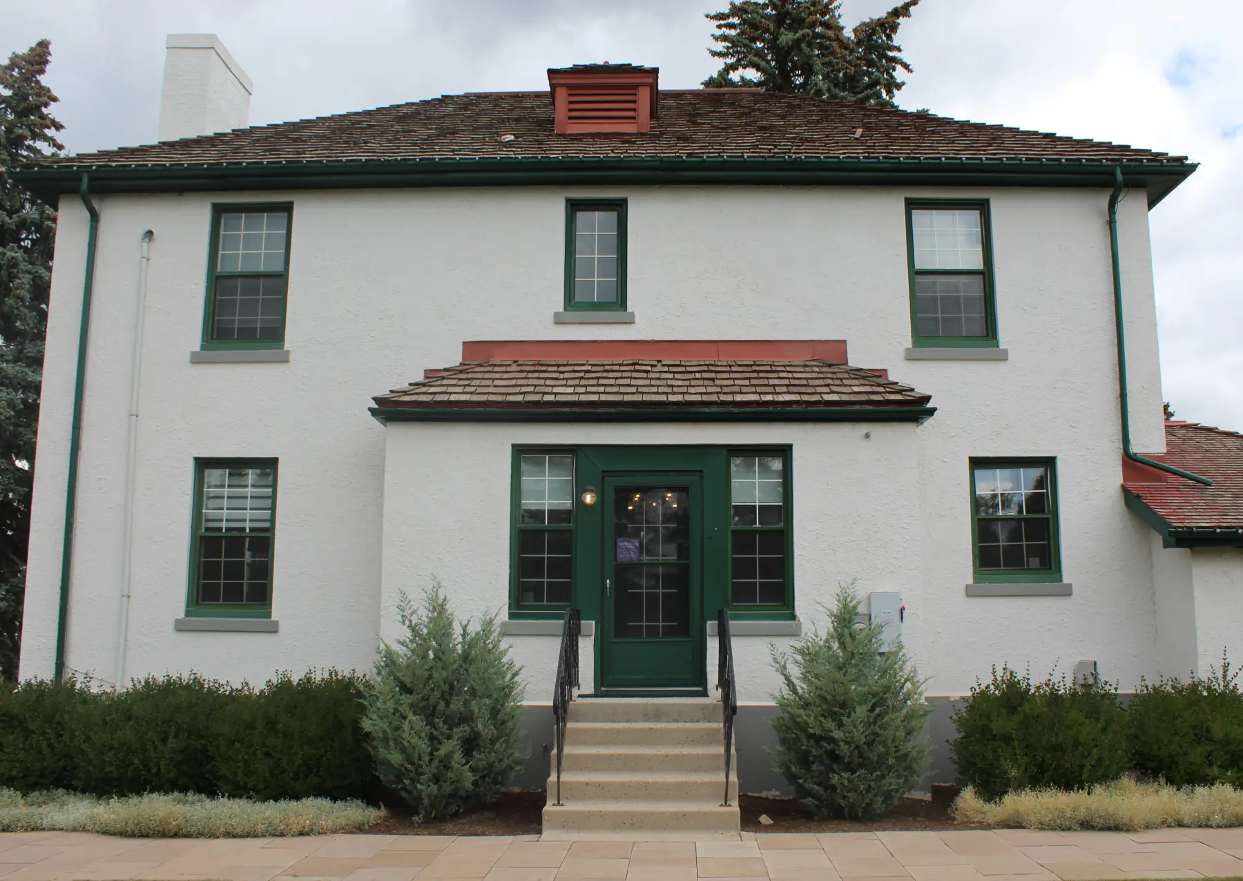 The Centre for Wholeness & Well Being — a white two-storey house with a green front door and landscaped grounds in Currie, Calgary.